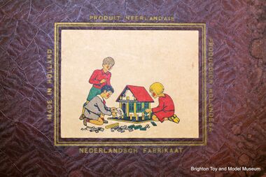 Mobaco sticker used on the lower-left corner of the box lid, showing an illustration of three children using the system to build a model house. The sticker is surrounded by the text "MADE IN HOLLAND" / "NEDERLANDSCH FABRIKAAT" / "PRODUIT NEEDLANDAIS" / "PRODUCCION HOLLANDESA"