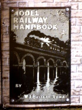 Cover of the Model Railway Handbook, executed as a miniature enamelled tinplate advertising poster, as a trackside accessory for gauge 0 model railways (Bassett-Lowke Ltd.)